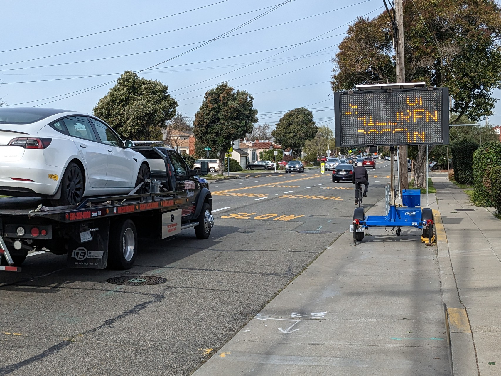 A man cycling eastbound on Otis Drive with a tow truck about to overtake him.